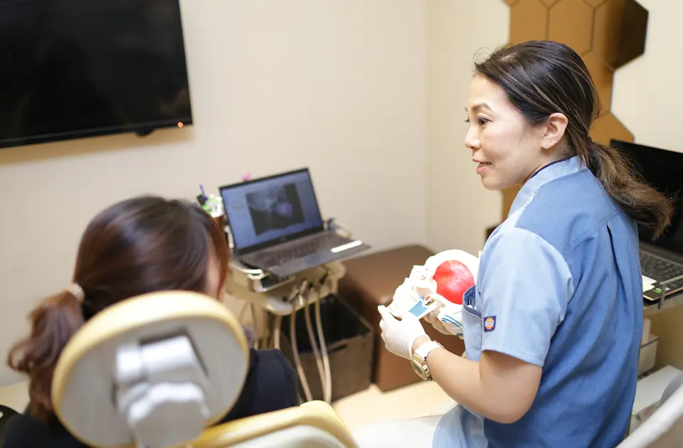日本の歯科医院にて、顎の模型を使って顎関節症の原因を丁寧に説明する歯科医師